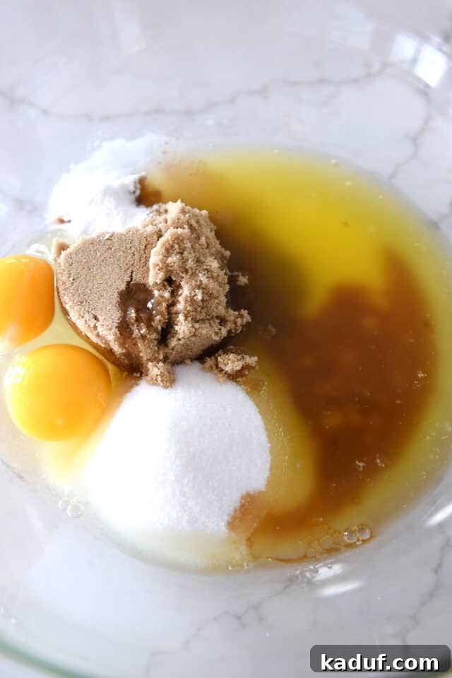 Golden Oat Chocolate Chip Squares 3 Glass bowl with white sugar, brown sugar, egg, egg yolk, and melted butter, ready to be mixed for the cookie dough.