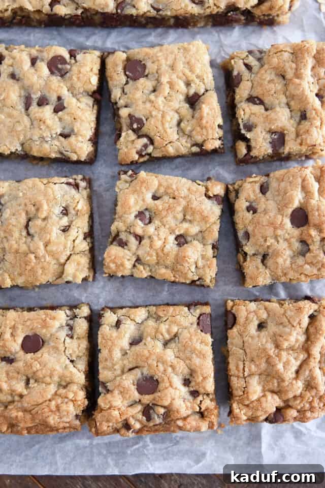 Golden Oat Chocolate Chip Squares 8 Nine cut squares of oatmeal chocolate chip cookie bars on white parchment paper, ready to be served.