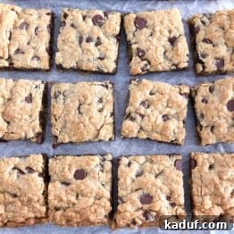 Twelve squares of cut chocolate chip cookie bars on white parchment paper, ready for serving.