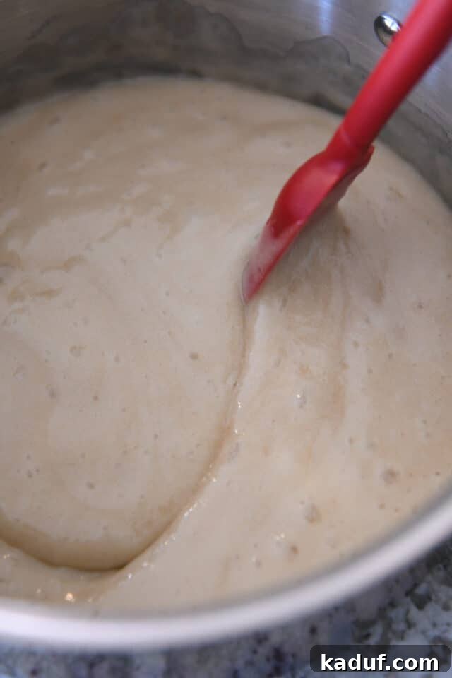 Sweet Tangy Buttermilk Caramel 6 Stirring syrup in saucepan with red spatula.