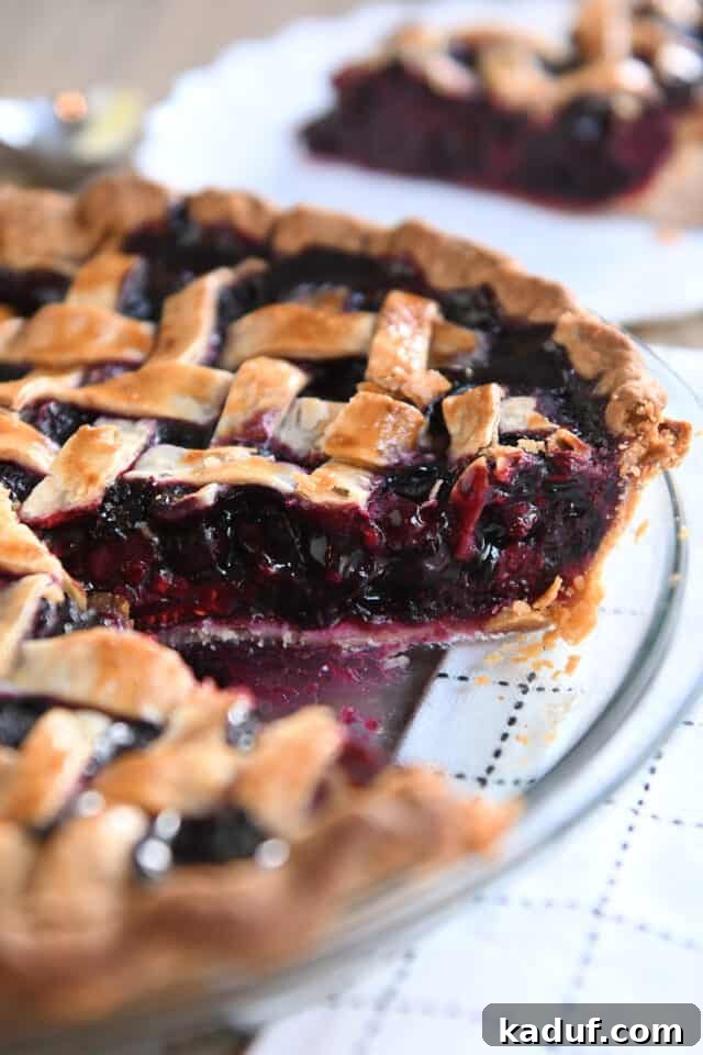 Berry Trio Bliss 2 A slice has been removed from a perfectly baked triple berry pie in a clear glass pie plate, revealing the vibrant, thick berry filling and golden lattice crust.