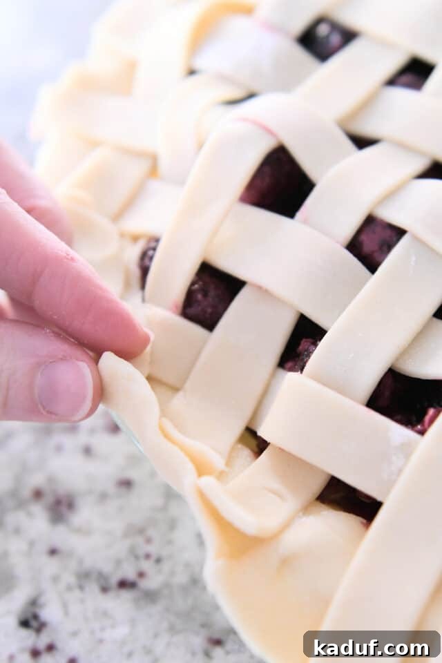 Berry Trio Bliss 5 The process of folding over the edge of a pie crust with a neatly arranged lattice top is shown, preparing it for fluting.