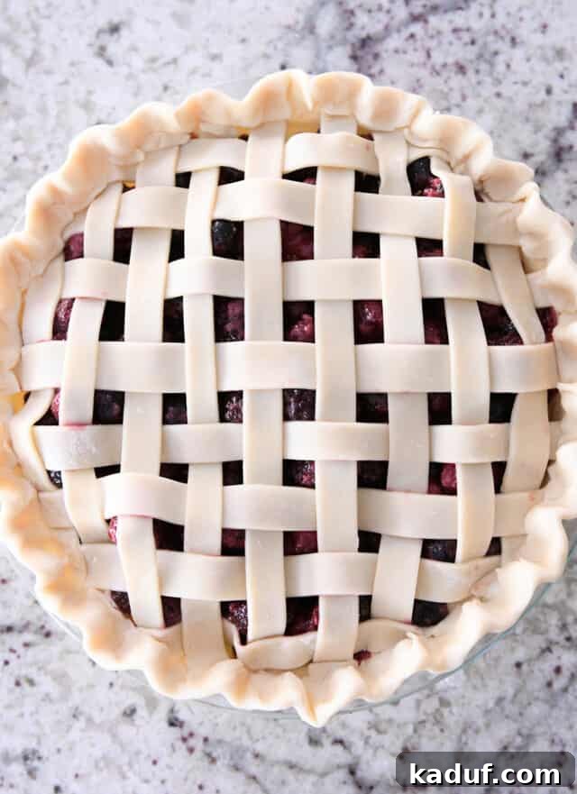 Berry Trio Bliss 6 An unbaked triple berry pie, showcasing its beautifully fluted edges and intricate lattice top, ready for the oven.