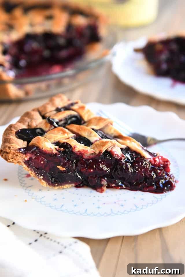 Berry Trio Bliss 8 A single, perfectly cut slice of triple berry pie rests on a elegant white scalloped plate, accompanied by a fork.
