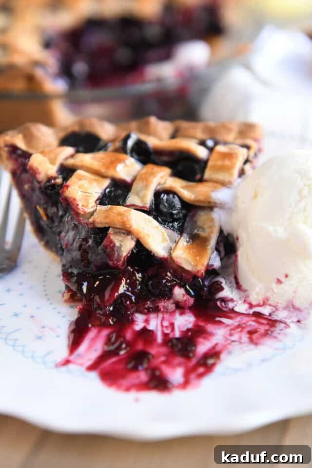Berry Trio Bliss 9 A bite has been taken from a slice of triple berry pie, served on a pristine white plate alongside a scoop of creamy vanilla ice cream.
