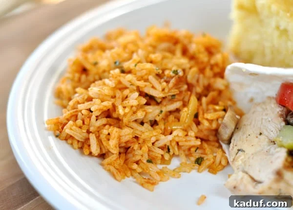 Fiesta Rice 3 A white plate featuring a generous scoop of vibrant Mexican rice, perfectly positioned next to a sizzling chicken fajita and a golden slice of cornbread.
