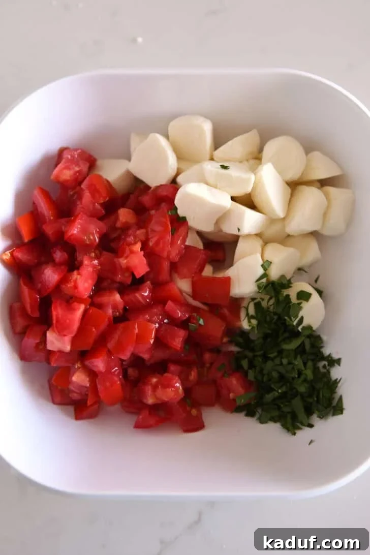 Effortless Caprese Salad 3 Top down view of a white dish with marinated chopped tomatoes, fresh mozzarella, and chopped basil.