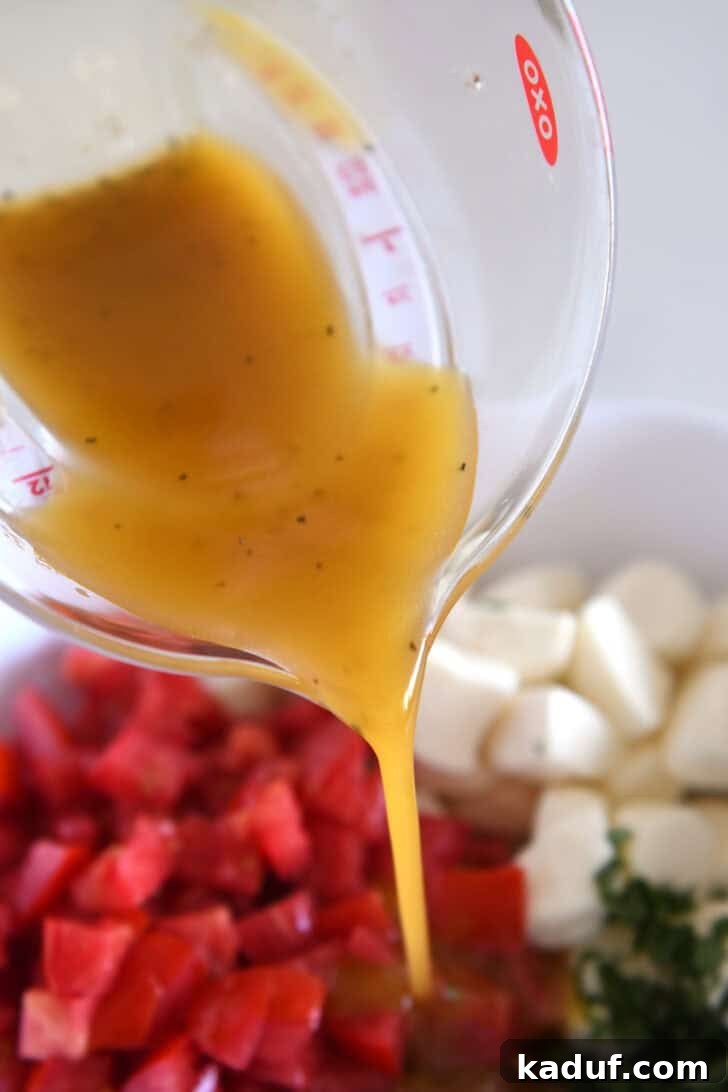 Effortless Caprese Salad 4 A glass measuring cup pouring an oil mixture into a white dish with chopped tomatoes and mozzarella.