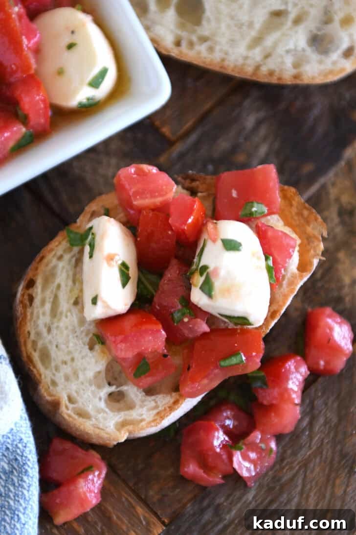 Effortless Caprese Salad 6 Top down view of a baguette slice with a tomato and mozzarella salad on top of the bread and spilling off the sides.