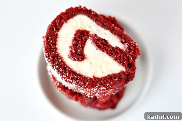 Crimson Velvet Swirl Cake 2 Slices of a red velvet cake roll with a cream cheese filling stacked on a white plate, showcasing its vibrant red color and creamy swirl.