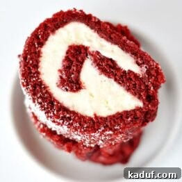 A vibrant red velvet cake roll on a white plate, showcasing its beautiful spiral filling.