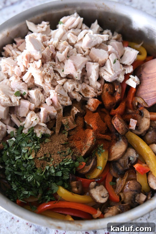 Pan filled with sauteed bell peppers, mushrooms, cilantro, cumin, chili powder, and cooked chicken.