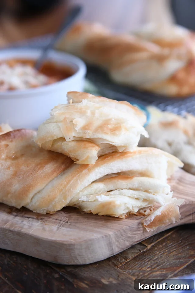 Effortless Twisted Croissant French Bread 13 Piece of croissant French bread on top of loaf on wood cutting board.