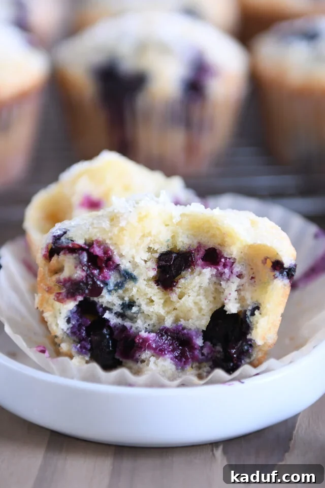 Ultimate Blueberry Muffins 9 A half-eaten baked blueberry muffin, revealing its moist interior and plump berries, served in a small white dish.