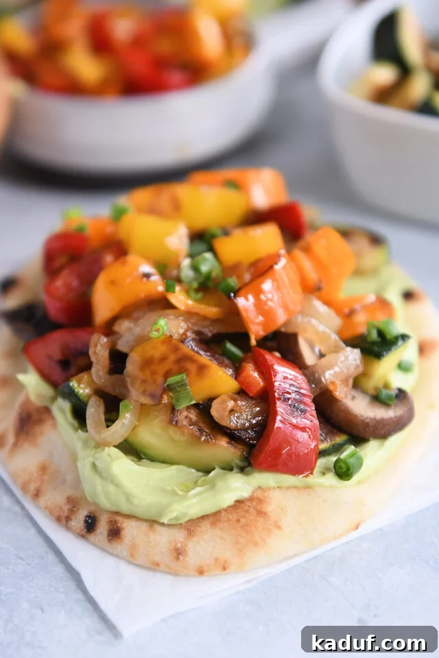 Garden Harvest Flatbread with Avocado Cream 2 Flatbread on white parchment paper topped with creamy avocado sauce and roasted vegetables.