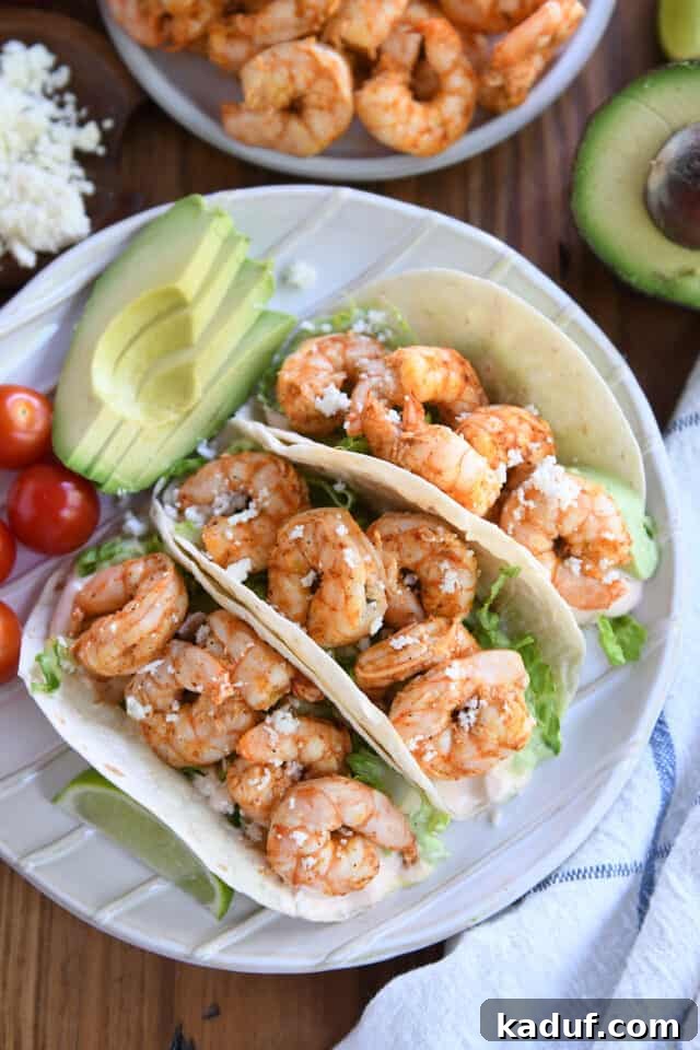 Zesty Chile Lime Shrimp Tacos 2 Three shrimp tacos on white plate with avocado and cherry tomato.