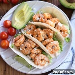 Zesty Chile Lime Shrimp Tacos 8 Three shrimp tacos on white ridged plate with tomatoes and avocado.