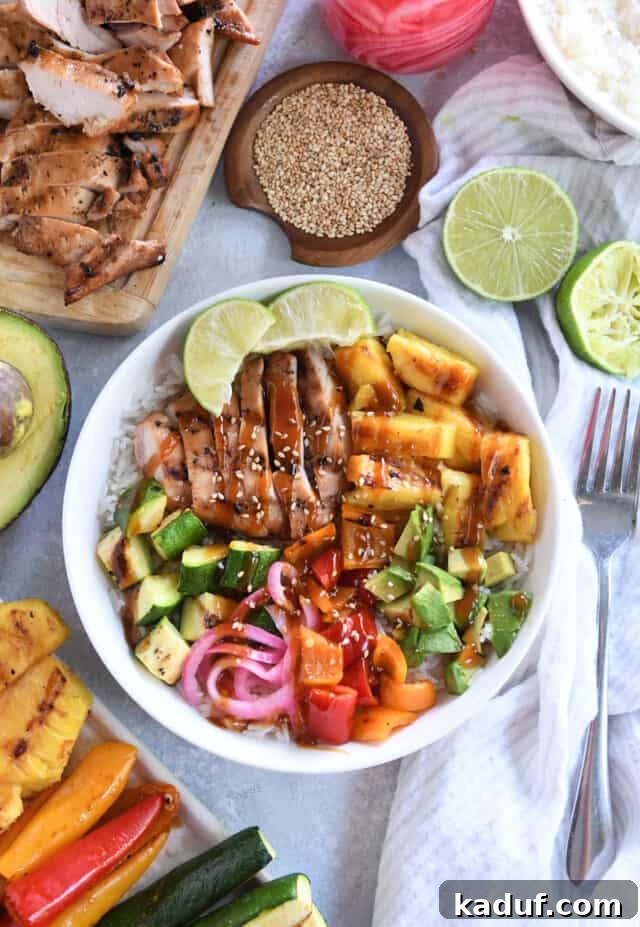 Tropical Chicken Teriyaki Power Bowl 2 A beautifully arranged white bowl filled with grilled teriyaki chicken, vibrant avocado slices, fresh lime wedges, golden pineapple chunks, and colorful bell peppers. The bowl is artfully surrounded by additional fresh limes, pickled red onions, and other tantalizing ingredients, showcasing the dish's freshness and appeal.