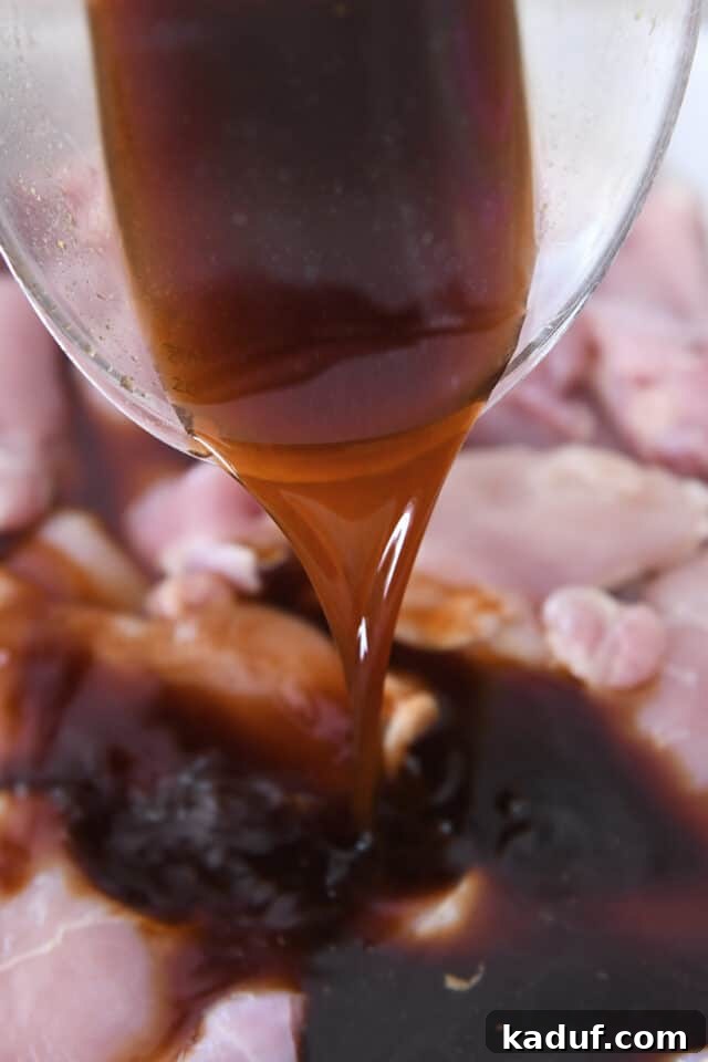 Tropical Chicken Teriyaki Power Bowl 3 A close-up shot of raw chicken pieces being generously coated with a rich, glossy teriyaki marinade, preparing them for an infusion of Hawaiian flavors.