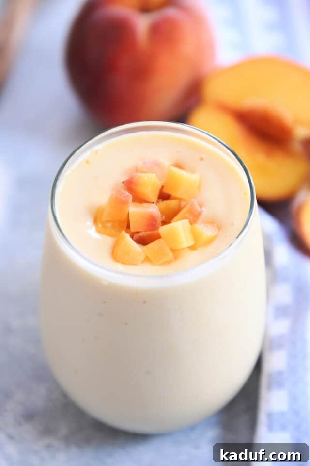 Golden Sunrise Peach Protein Smoothie 2 A vibrant Sunrise Peach Orange Protein Smoothie in a clear glass, garnished with fresh peach chunks, set against a backdrop of fresh peaches.