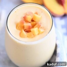 Golden Sunrise Peach Protein Smoothie 6 A beautiful Sunrise Peach Orange Protein Smoothie in a glass, garnished with fresh peach pieces.