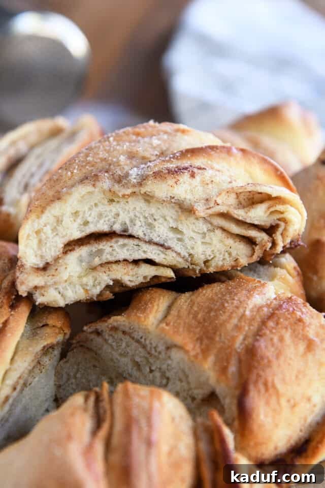 Flaky Cinnamon Croissant Swirl 2 A slice of golden-brown cinnamon sugar twisted croissant bread, showing its distinct flaky layers, resting on a serving board with other pieces.