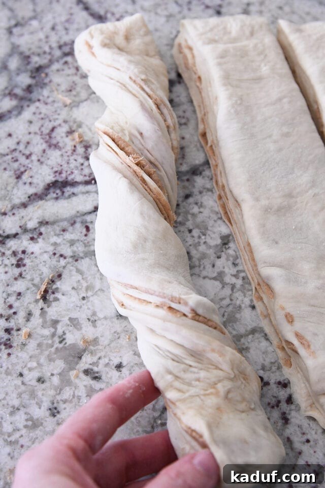Flaky Cinnamon Croissant Swirl 17 A strip of cinnamon sugar croissant bread dough being twisted carefully, creating the signature spiral shape.