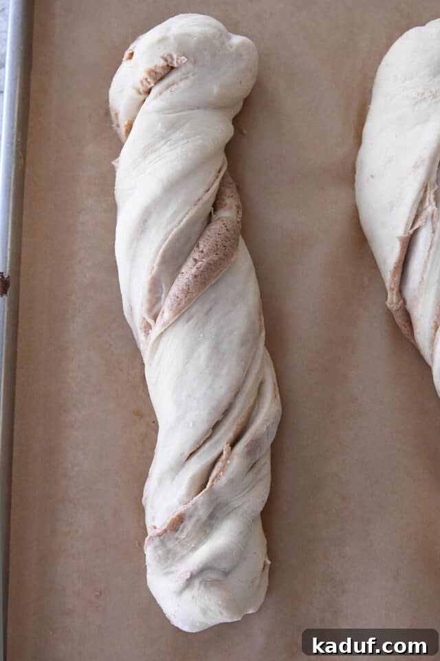 Flaky Cinnamon Croissant Swirl 18 An unbaked loaf of twisted croissant bread, noticeably puffy and ready for the oven, resting on brown parchment paper.