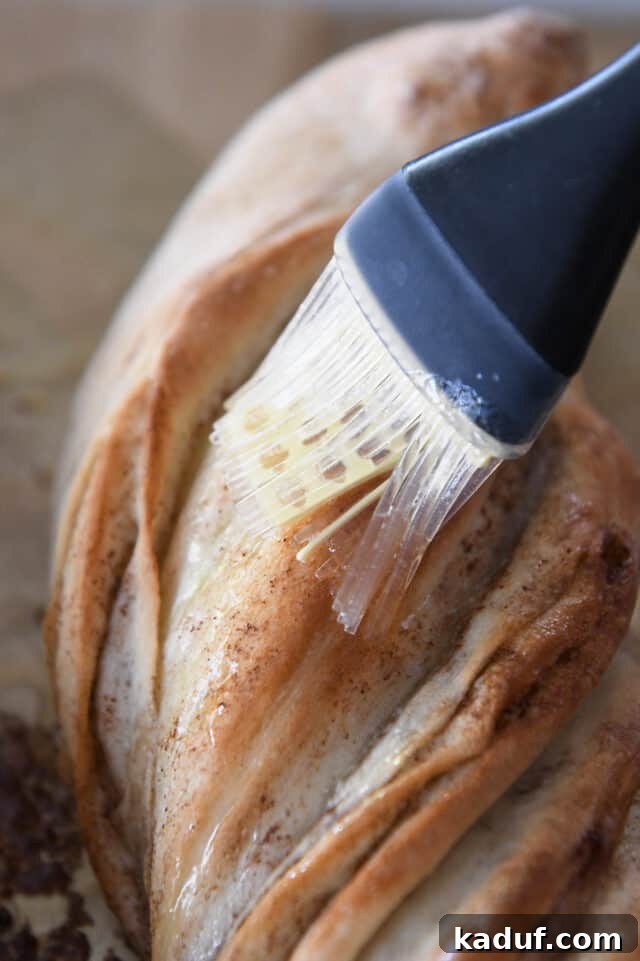 Flaky Cinnamon Croissant Swirl 20 A pastry brush applying melted butter from the baking sheet onto the warm, baked twisted croissant bread.