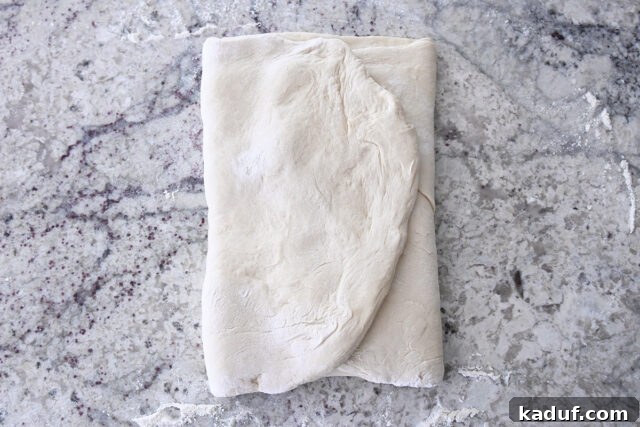 Flaky Cinnamon Croissant Swirl 7 French bread dough partially folded over the butter packet on a lightly floured counter, showing the initial layering step.