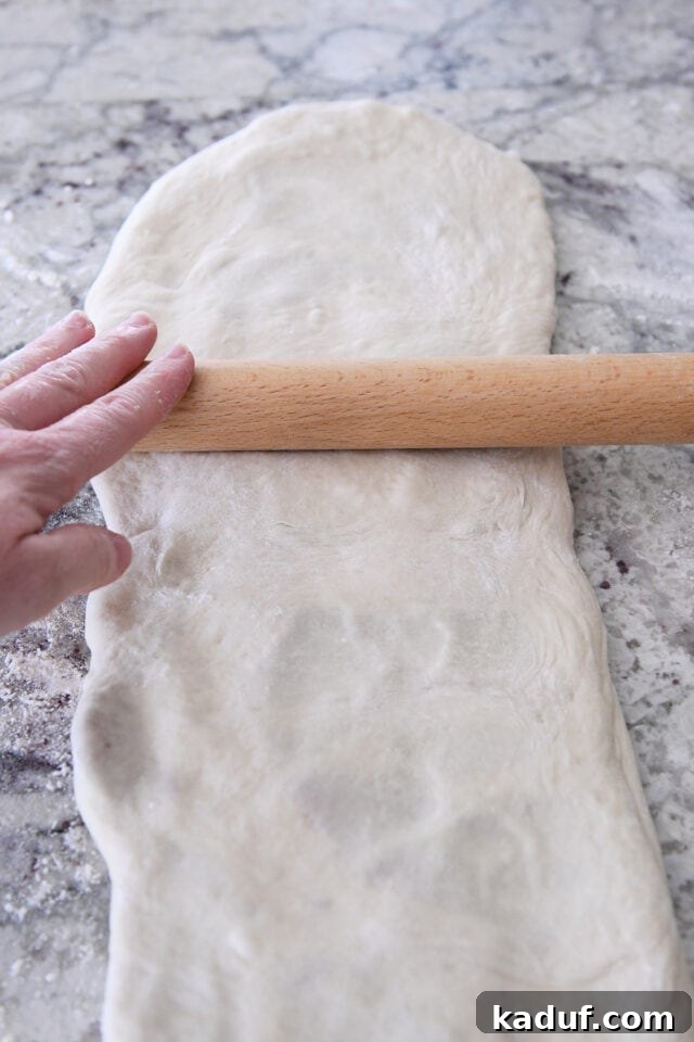Flaky Cinnamon Croissant Swirl 10 Rolling the croissant bread dough into a very long, thin rectangle on a floured surface, demonstrating the second rolling step.
