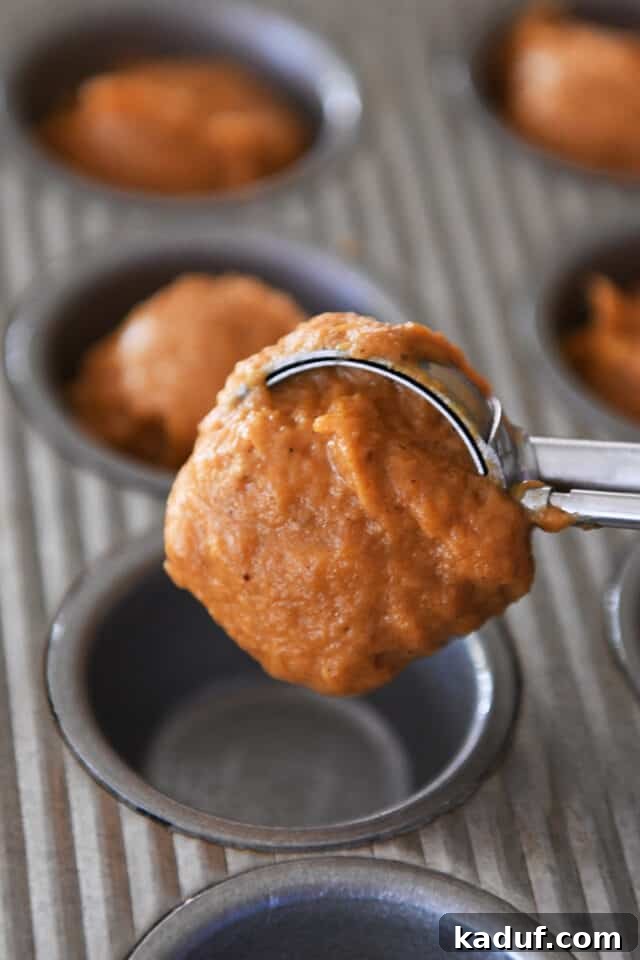 Pumpkin Donut Muffin Bites 6 A cookie scoop precisely portioning pumpkin muffin batter into a mini muffin tin, ensuring even sizes.