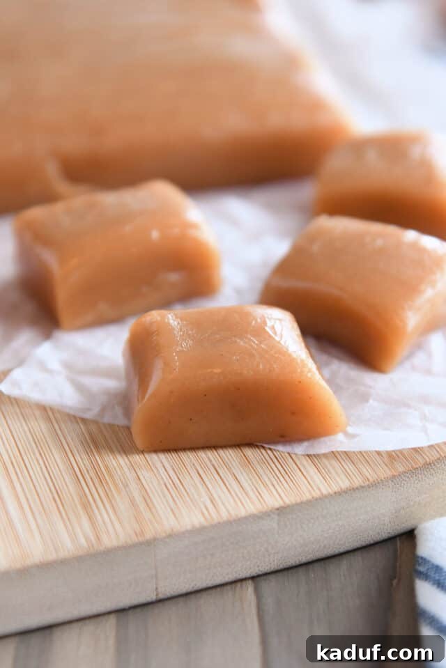 Orchard Cider Caramels 3 Three squares of golden brown apple cider caramels meticulously arranged on parchment paper.