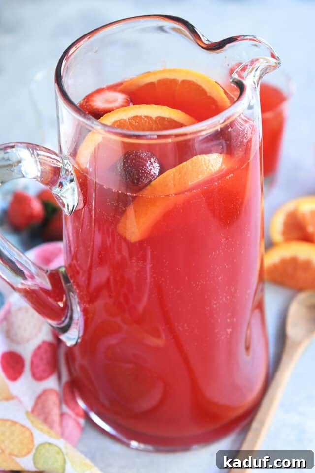 Party Punch Perfection 2 Red party punch in a clear glass pitcher, garnished with fresh orange slices and vibrant red strawberries, ready to be served at an event.