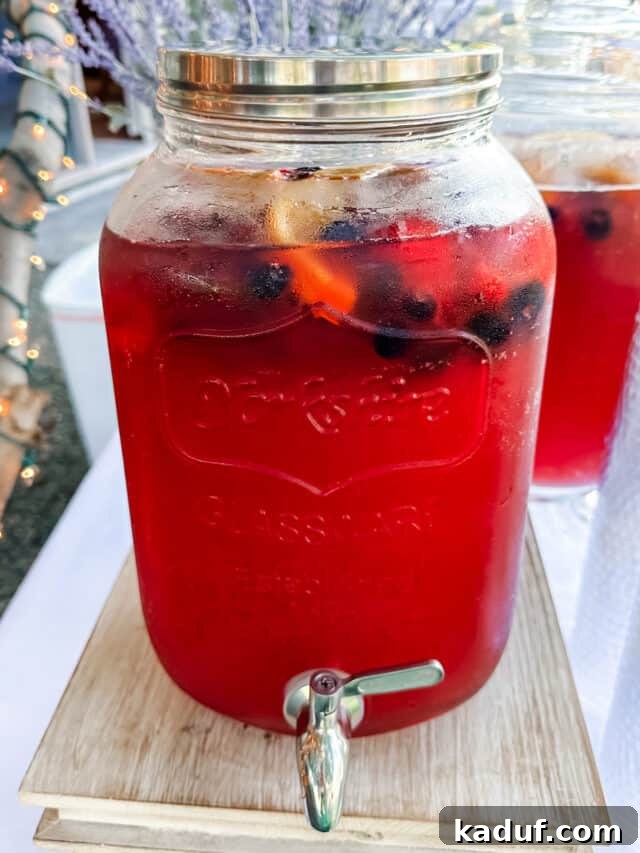 Party Punch Perfection 5 A two-gallon clear drink dispenser filled with vibrant red party punch, beautifully garnished with an assortment of fresh berries and citrus slices, ready for guests.