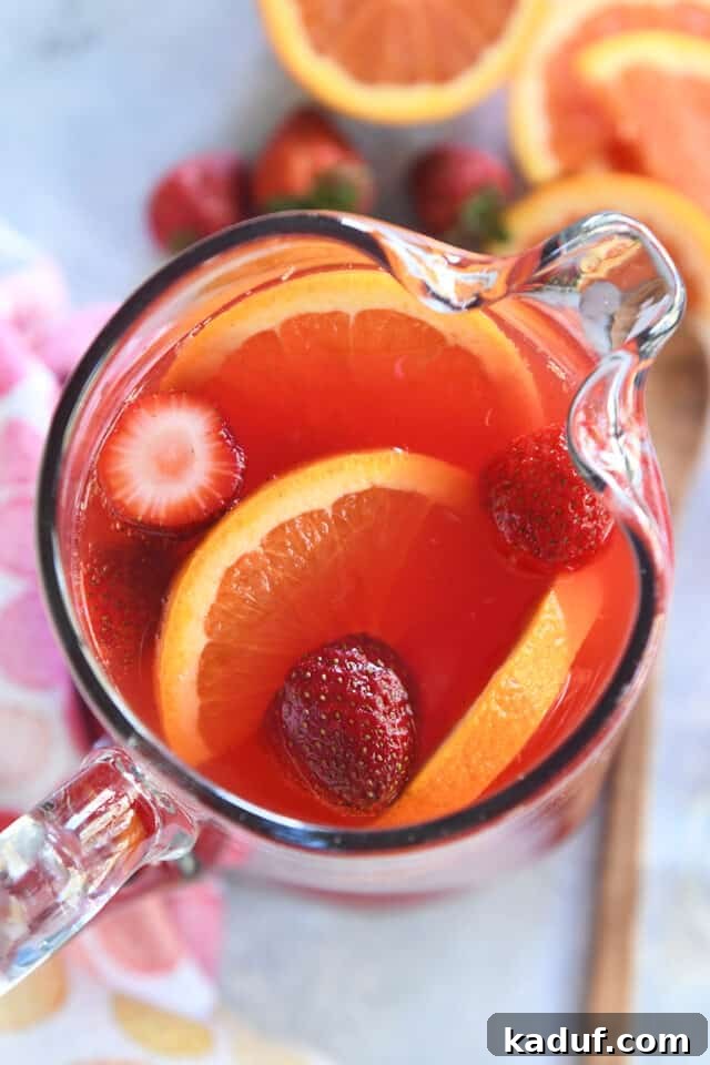 Party Punch Perfection 6 Overhead view of a glass pitcher filled with vibrant red party punch, elegantly garnished with fresh orange slices and whole strawberries, ready for serving.