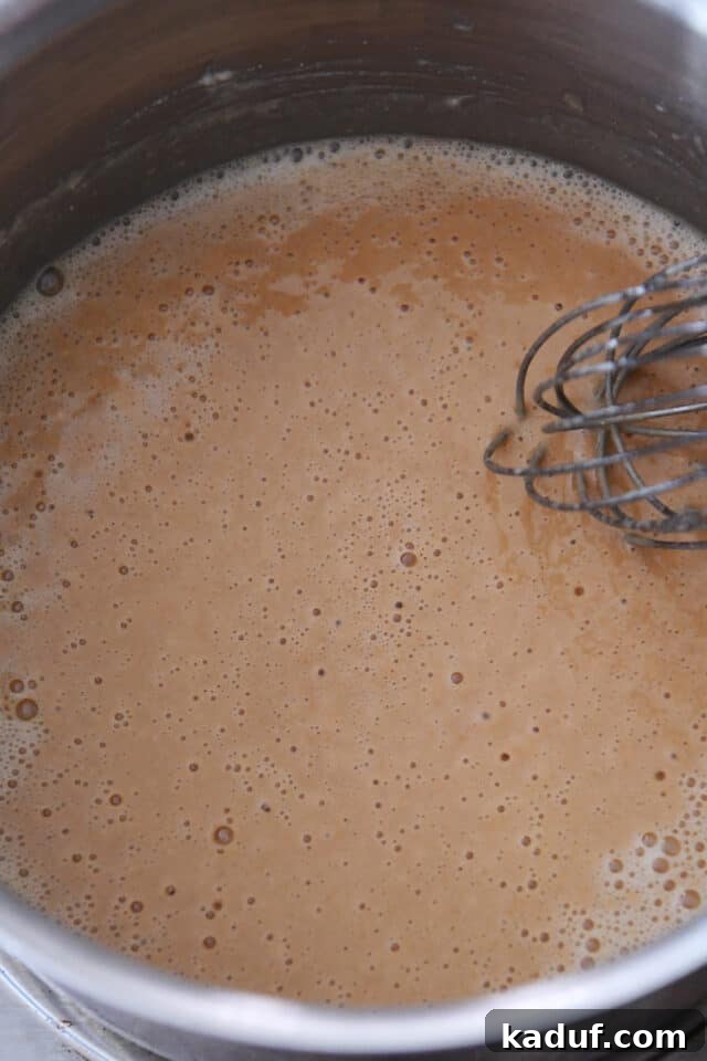 Roux cooking to a golden color in a pan, stirred with a whisk.