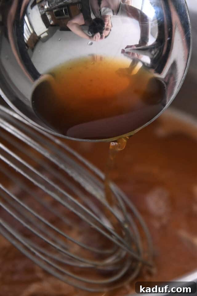 Adding hot broth to a pan of cooking roux for gravy.