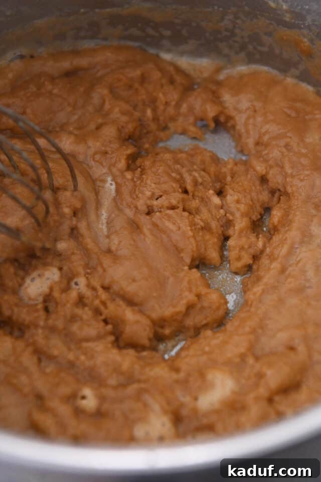 Close-up of roux mixing with broth in a saucepan, beginning to thicken.