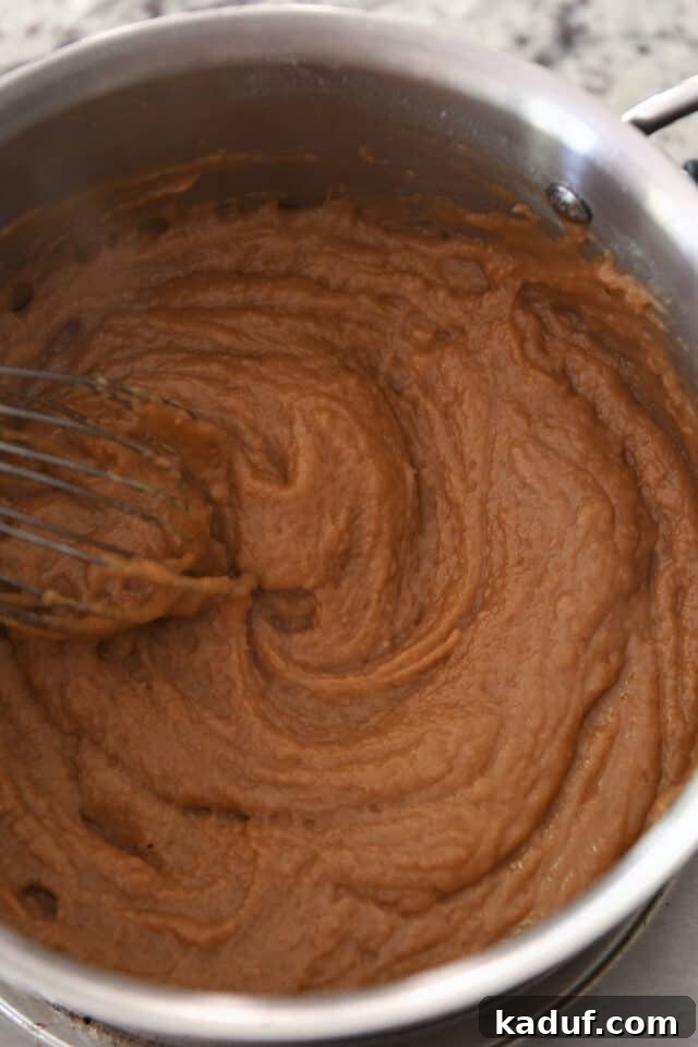 Vigorously whisking roux and broth in a saucepan to prevent lumps.