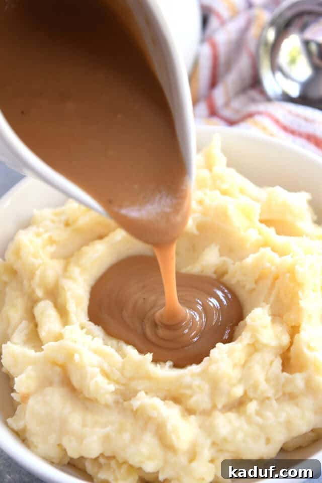 Pouring rich brown gravy from a gravy boat onto a mound of fluffy mashed potatoes.