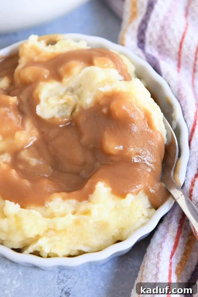 A white dish featuring fluffy mashed potatoes with a generous serving of brown gravy and a spoon.