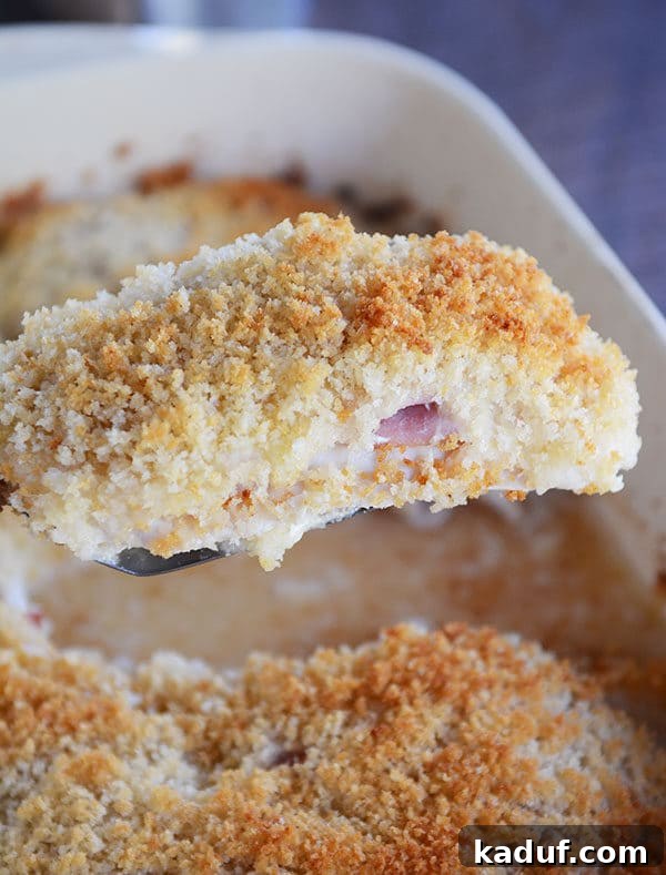 Gourmet Chicken Cordon Bleu Made Simple 2 A golden-brown breaded chicken cordon bleu cutlet being lifted from a casserole dish, revealing its cheesy, ham-filled interior.