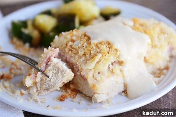 Gourmet Chicken Cordon Bleu Made Simple 3 A baked chicken cordon bleu portion in a casserole dish, generously drizzled with a creamy white sauce, with a bite taken out.