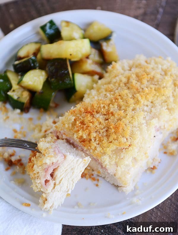 Gourmet Chicken Cordon Bleu Made Simple 4 A baked chicken cordon bleu portion, with a fork taking a bite, served with a side of sautéed zucchini.