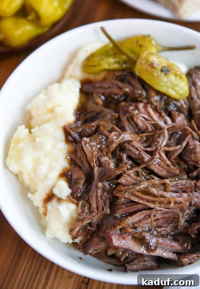 Homemade Mississippi Pot Roast 2 White bowl with fluffy mashed potatoes, succulent shredded Mississippi pot roast, rich gravy, and vibrant pepperoncini.