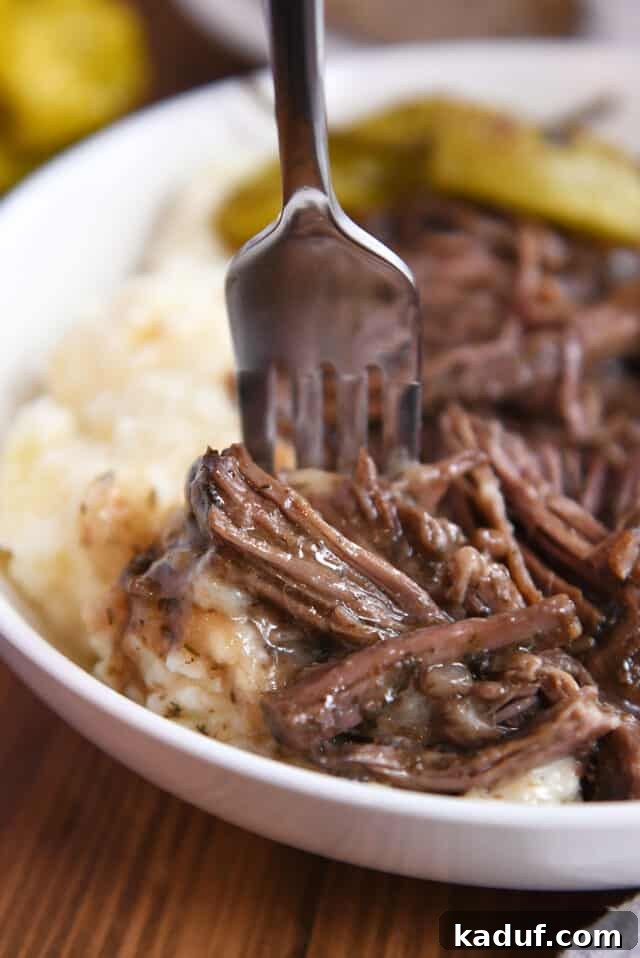 Homemade Mississippi Pot Roast 3 A fork piercing tender shredded beef and gravy, with mashed potatoes in the background.