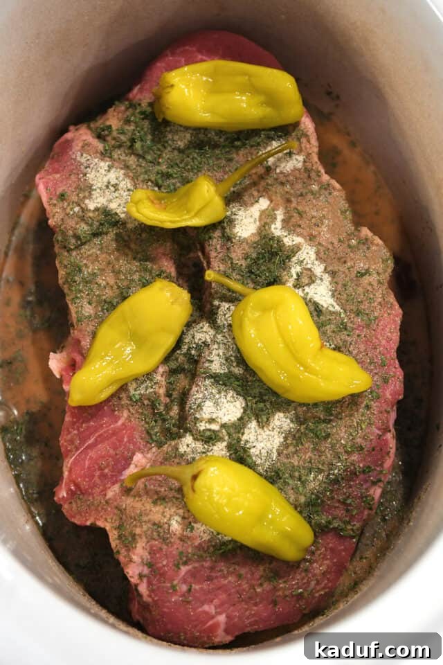 Homemade Mississippi Pot Roast 4 Raw chuck roast in a slow cooker insert, surrounded by pepperoncini, a blend of seasonings, and beef broth.