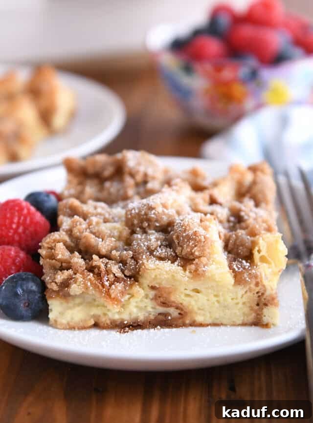 Square serving of French toast bake on white plate with fresh berries and powdered sugar.