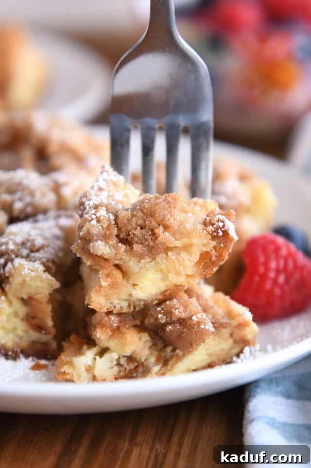 Fork skewering two bites of baked French toast on white plate.